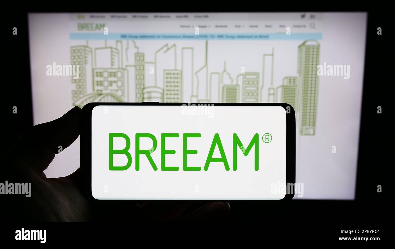 Personne tenant un smartphone avec logo de certification de bâtiment vert BREEAM à l'écran devant le site Web. Mise au point sur l'affichage du téléphone. Banque D'Images