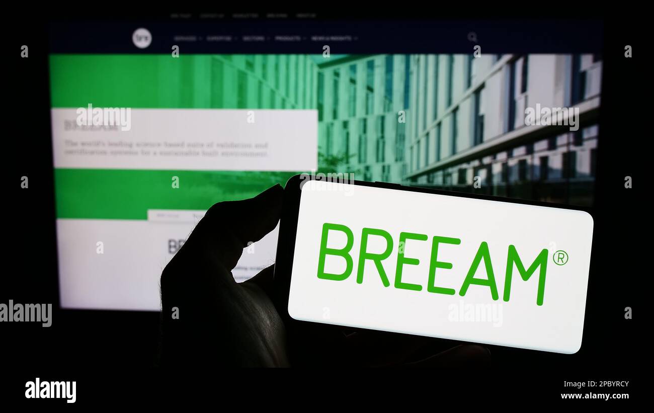 Personne tenant un téléphone mobile avec logo de certification de bâtiment vert BREEAM à l'écran en face de la page Web. Mise au point sur l'affichage du téléphone. Banque D'Images