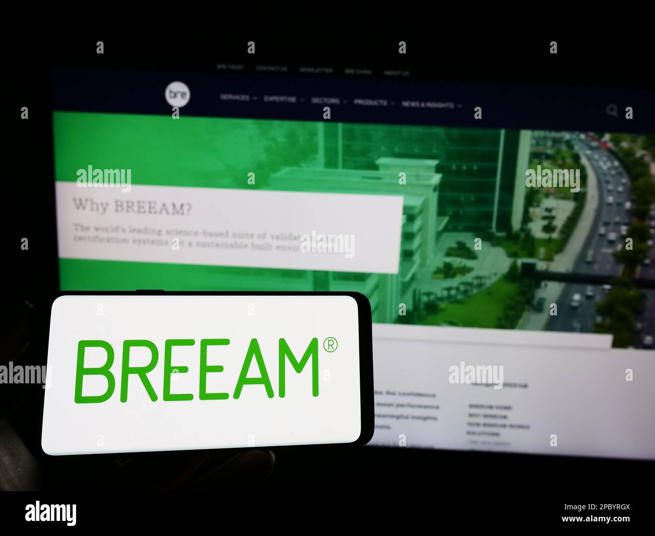 Personne tenant un téléphone portable avec logo de certification de bâtiment vert BREEAM à l'écran en face de la page Web. Mise au point sur l'affichage du téléphone. Banque D'Images