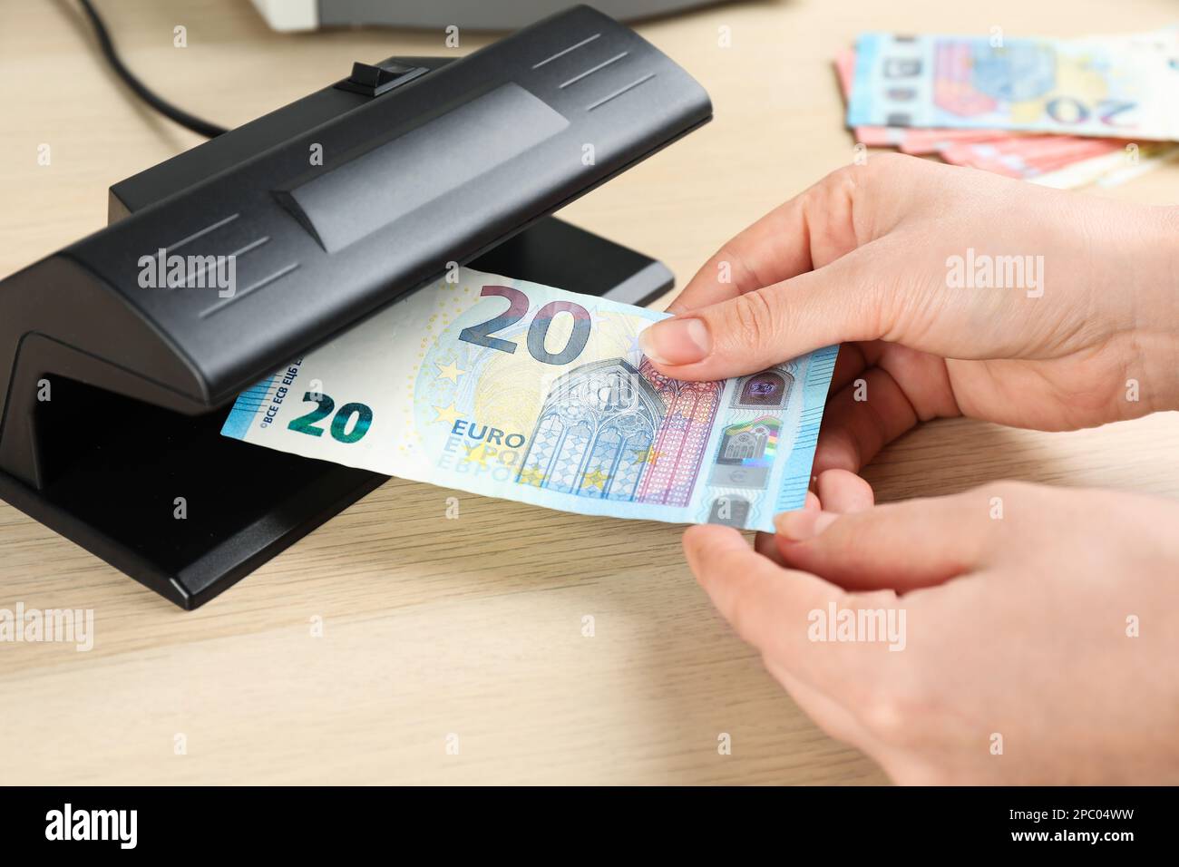 Femme vérifiant un billet d'euro avec détecteur de devises à une table en bois, gros plan. Appareil d'examen de l'argent Banque D'Images