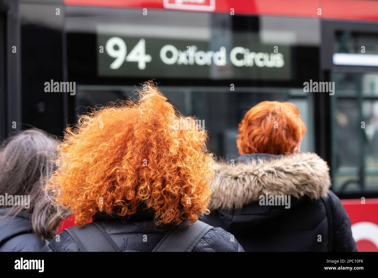 Des piétons à tête rouge font la queue pour un bus sur Oxford Street, Londres, Angleterre, Royaume-Uni Banque D'Images