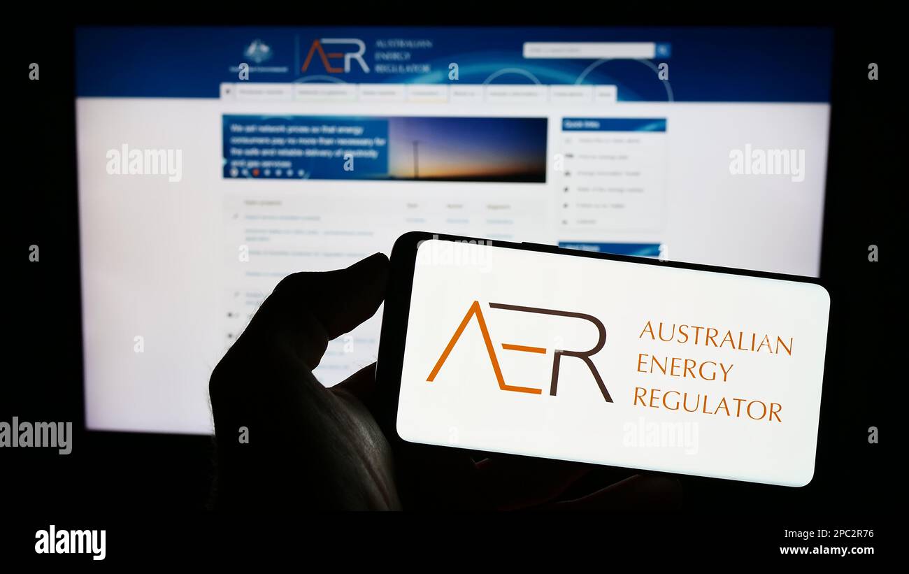 Personne tenant un téléphone portable avec le logo de l'autorité Australian Energy Regulator (AER) à l'écran devant la page Web. Mise au point sur l'affichage du téléphone. Banque D'Images