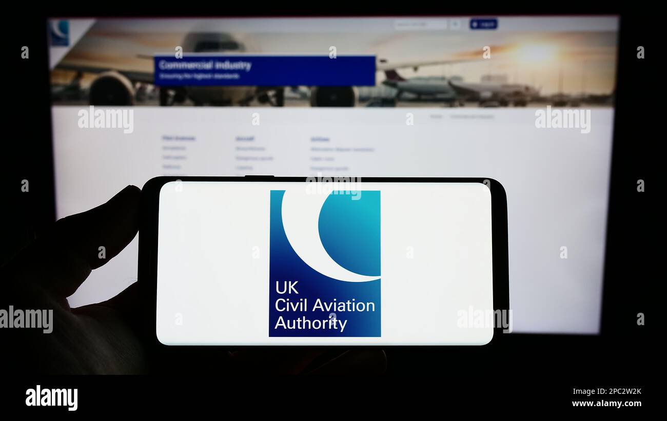 Personne tenant un téléphone portable avec le logo de l'autorité de  réglementation britannique de l'aviation civile (CAA) à l'écran en face de  la page Web. Mise au point sur l'affichage du téléphone