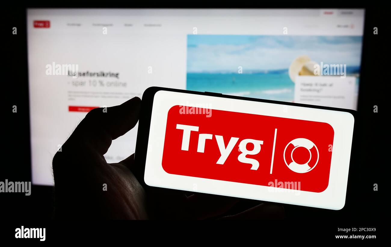 Personne tenant un téléphone portable avec le logo de la compagnie d'assurance danoise Tryg Forsikring COMME à l'écran en face de la page web d'affaires. Mise au point sur l'affichage du téléphone. Banque D'Images