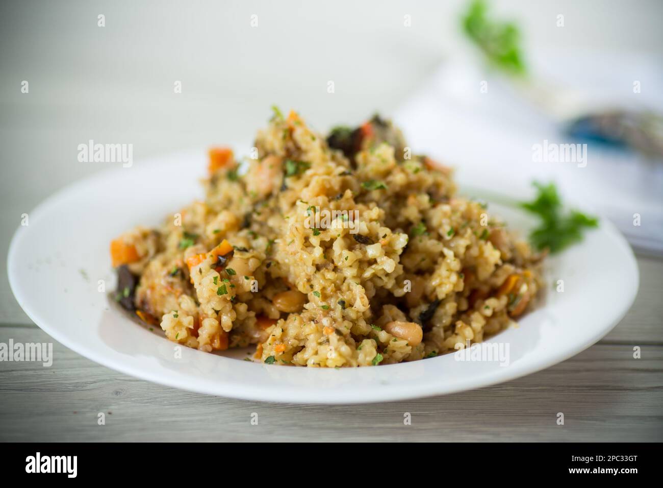 boulgour cuit avec des légumes, des carottes et des champignons séchés dans une assiette sur une table en bois. Banque D'Images