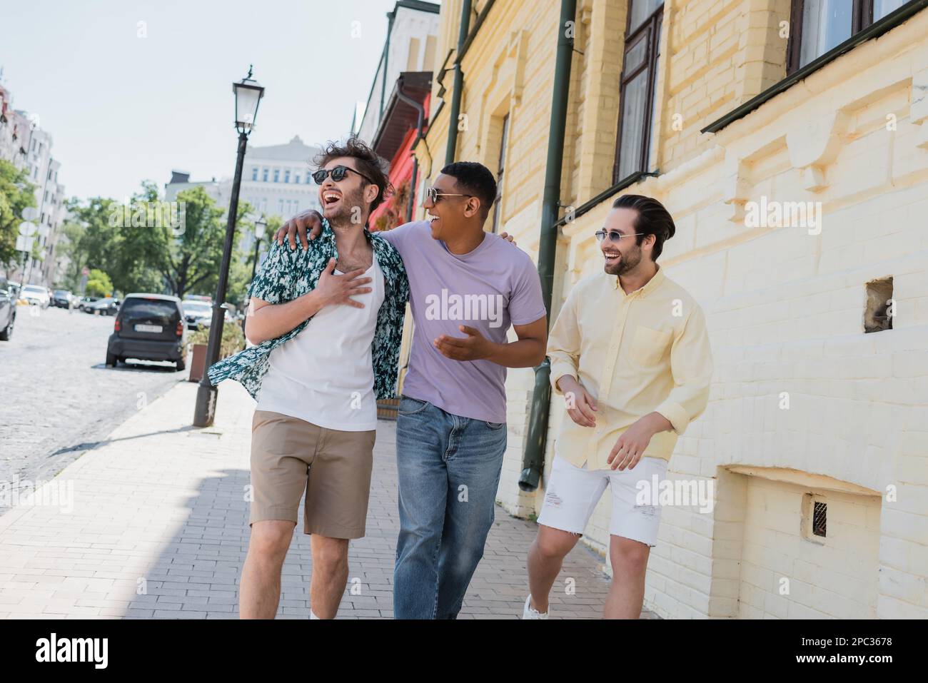 Amis multiethniques positifs dans des lunettes de soleil embrassant et marchant sur Andrews descente à Kiev, image de stock Banque D'Images