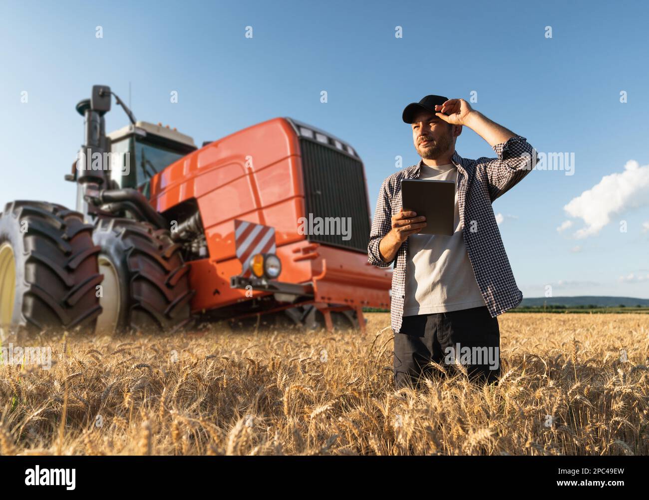 Agriculteur équipé d'une tablette numérique à l'arrière-plan d'un tracteur agricole Banque D'Images