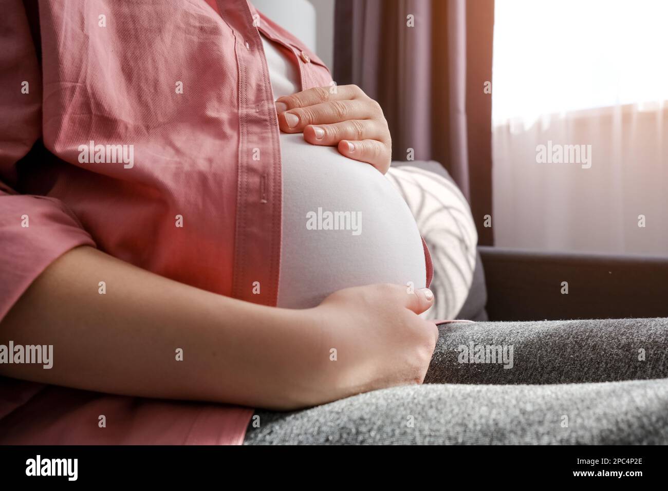 Gros plan de la jeune femme enceinte aimante assise sur un canapé qui couvre le grand ventre, exprimant l'amour et le soin à bébé à naître, en attendant l'accouchement, en se sentant dix Banque D'Images