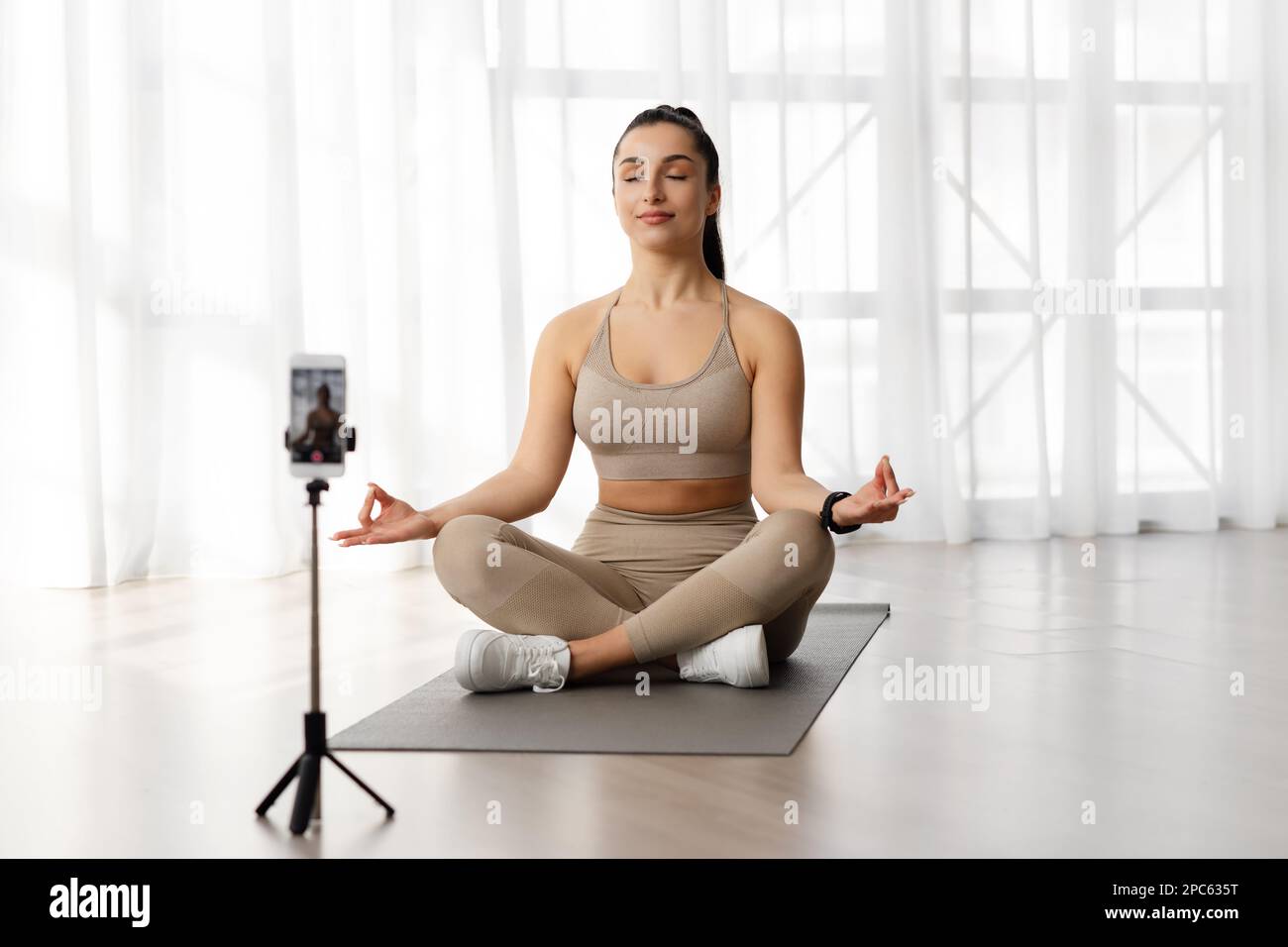 Femme paisible instructeur de yoga méditant et enregistrant la vidéo sur smartphone Banque D'Images
