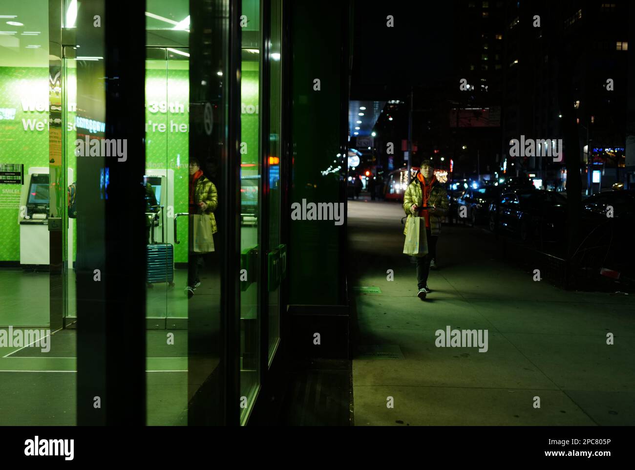 Une jeune femme passe devant le hall d'un guichet automatique d'une banque à New York la nuit Banque D'Images