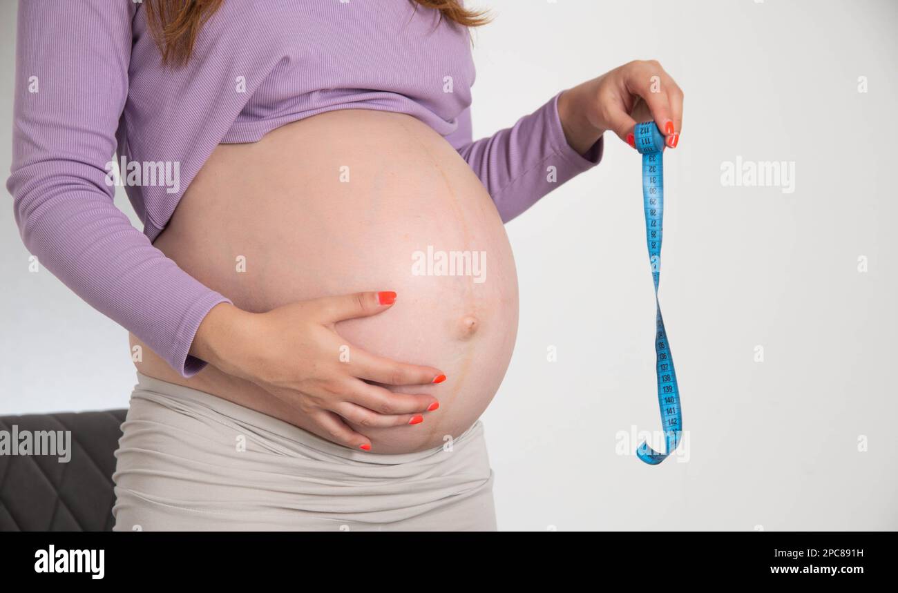 Une fille enceinte avec un grand ventre tient un mètre ruban sur un fond blanc. Le concept de mesure et de taille de l'abdomen pendant la grossesse. TH Banque D'Images