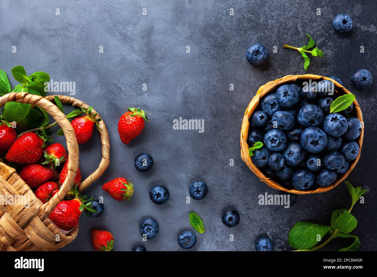 Myrtille et fraise biologiques fraîches avec feuilles de menthe dans un mini-panier sur table sombre vintage. Concept de saine alimentation. Vue de dessus, espace de copie. Banque D'Images