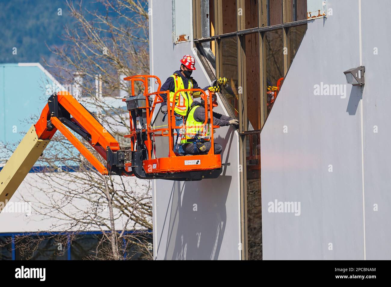 Deux hommes dans des gilets haute visibilité et des casques de sécurité sur un ascenseur installant des fenêtres dans un bâtiment commercial. Port Coquitlam, B. C., Canada. Banque D'Images