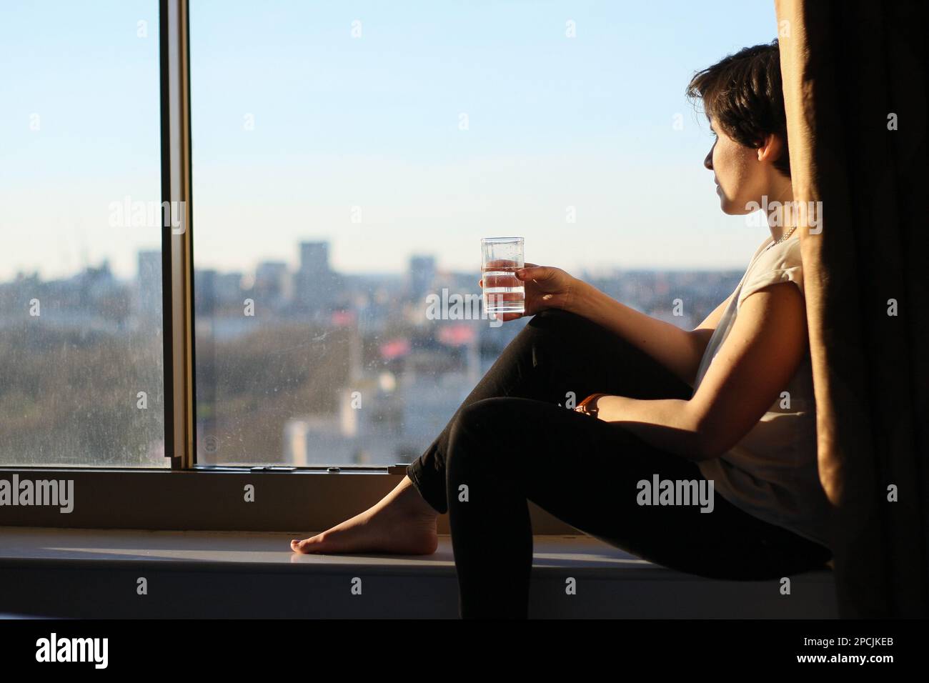Fille tenant un verre d'eau regardant par la fenêtre Banque D'Images