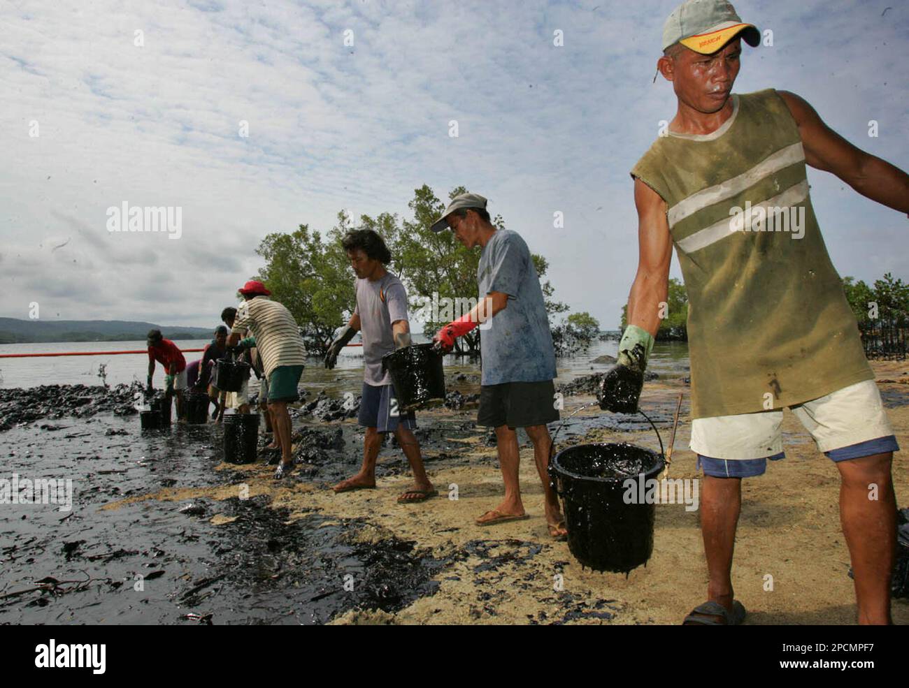 Workers pass on buckets of collected bunker oil from the shore line as they step up its cleaning activity Friday, Aug. 18, 2006 in Guimaras island in central Philippines. A tanker with 2 million liters of bunker oil sunk in the sea last Friday as officials were trying to avoid a major oil spill and to prevent the ravaged of fisheries and other coastal resources in one of the countries poorest province. (AP Photo/Pat Roque) Banque D'Images
