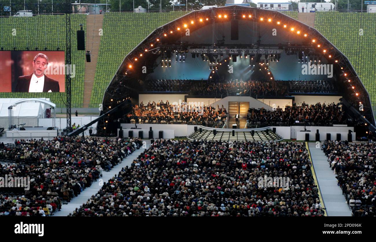 Spectators crowd around the stage with the three Munich orchestras performing with singer Placido Domingo on the screen left and stage, center, during an open-air concert with classical music in an event for the 2006 World Cup in the Olympic stadium in Munich, southern Germany, Tuesday, June 6, 2006. Olympic Stadium hosts the first game of the competition as host Germany plays Costa Rica, Friday, June 9. (AP Photo/Diether Endlicher) Banque D'Images