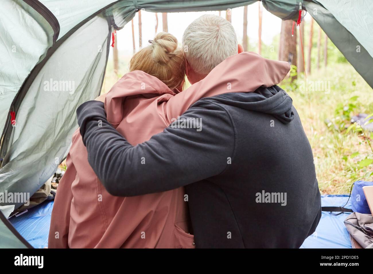 Vue arrière du couple senior avec les bras autour de se détendre dans la tente pendant le camping en forêt Banque D'Images Vue arrière du couple senior avec les bras autour de se détendre dans la tente pendant le camping en forêt Banque D'Images
