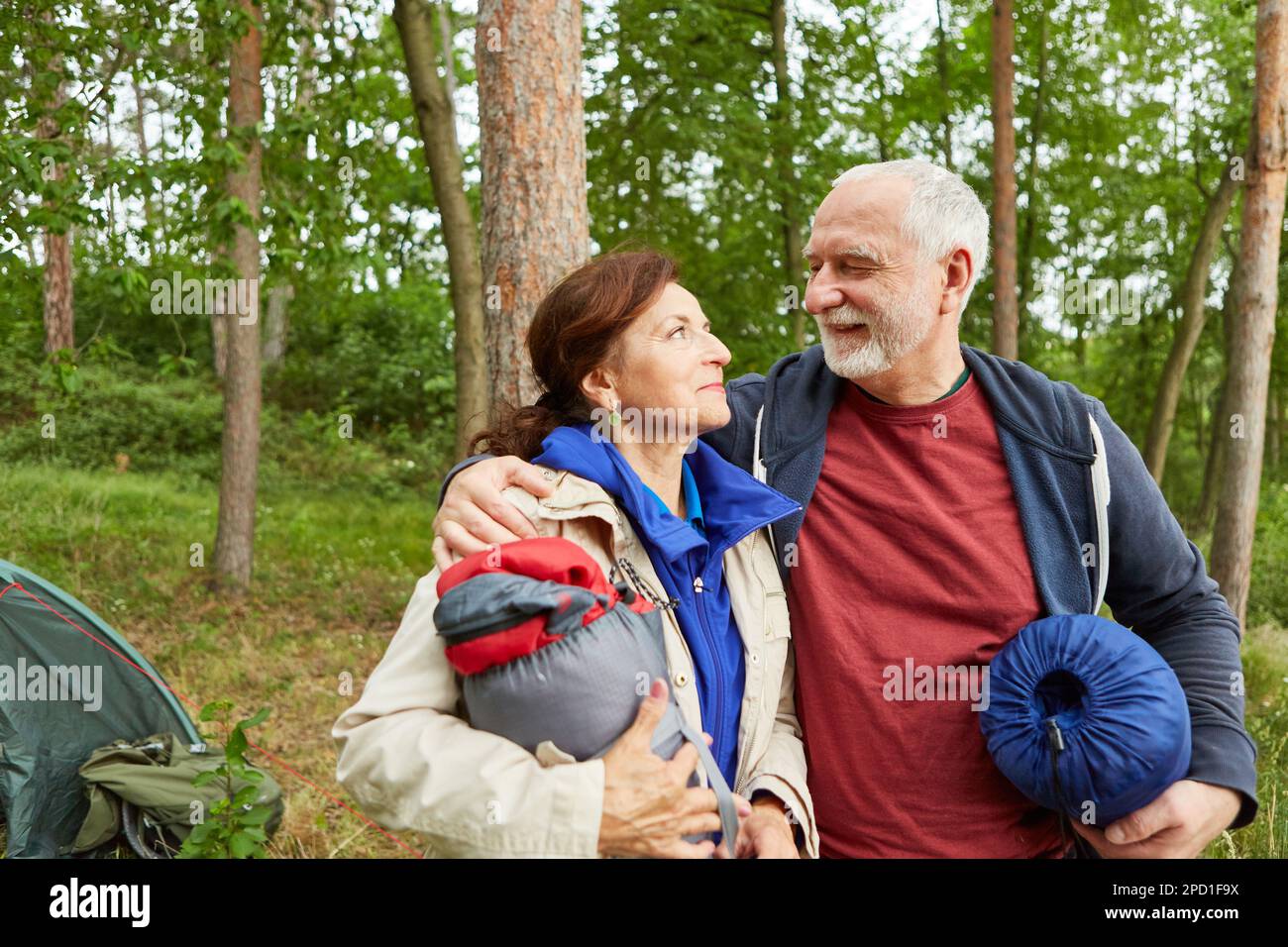 Homme âgé souriant avec bras autour de la femme tenant une tente dans la forêt pendant les vacances Banque D'Images Homme âgé souriant avec bras autour de la femme tenant une tente dans la forêt pendant les vacances Banque D'Images