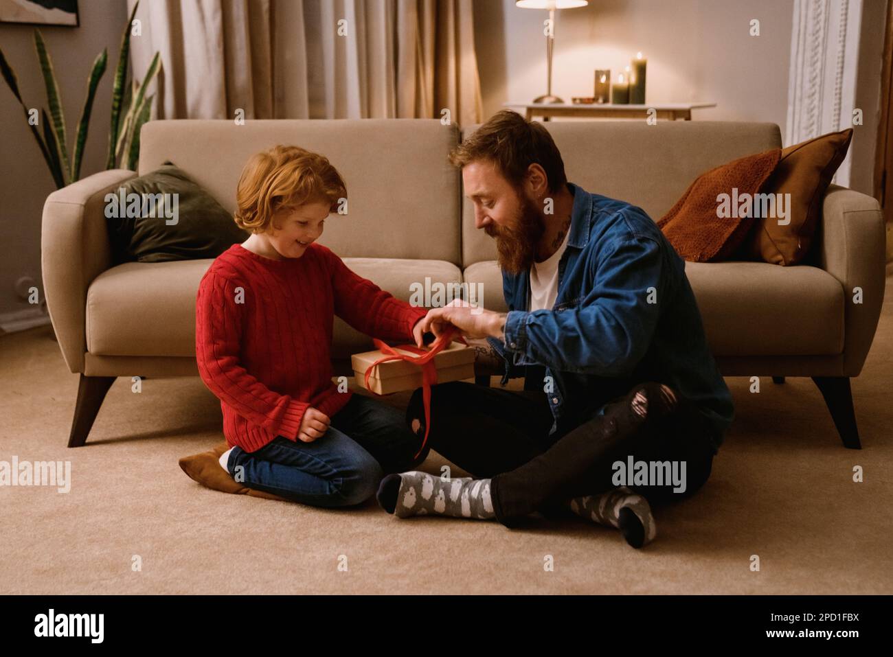 Le père et le petit fils se déparent du présent tout en étant assis sur le sol dans le salon confortable de la maison Banque D'Images