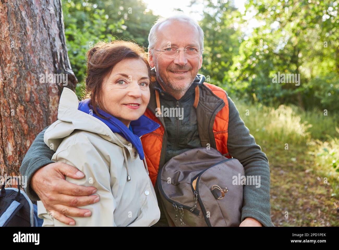 Portrait d'un couple senior souriant assis avec un sac à dos en forêt pendant les vacances d'été Banque D'Images Portrait d'un couple senior souriant assis avec un sac à dos en forêt pendant les vacances d'été Banque D'Images