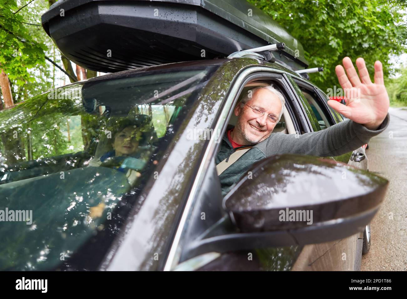 Portrait d'un homme âgé heureux qui agite la main tout en voyageant avec une femme en voiture pendant les vacances Banque D'Images