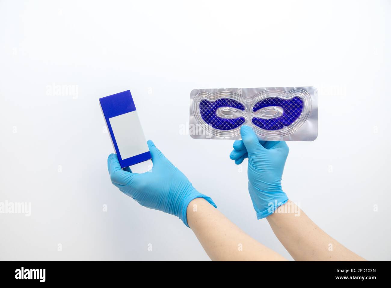 Gros plan main non reconnaissable dans des gants bleus tenir et présenter le masque facial en gel et crème sur fond blanc de studio. Banque D'Images