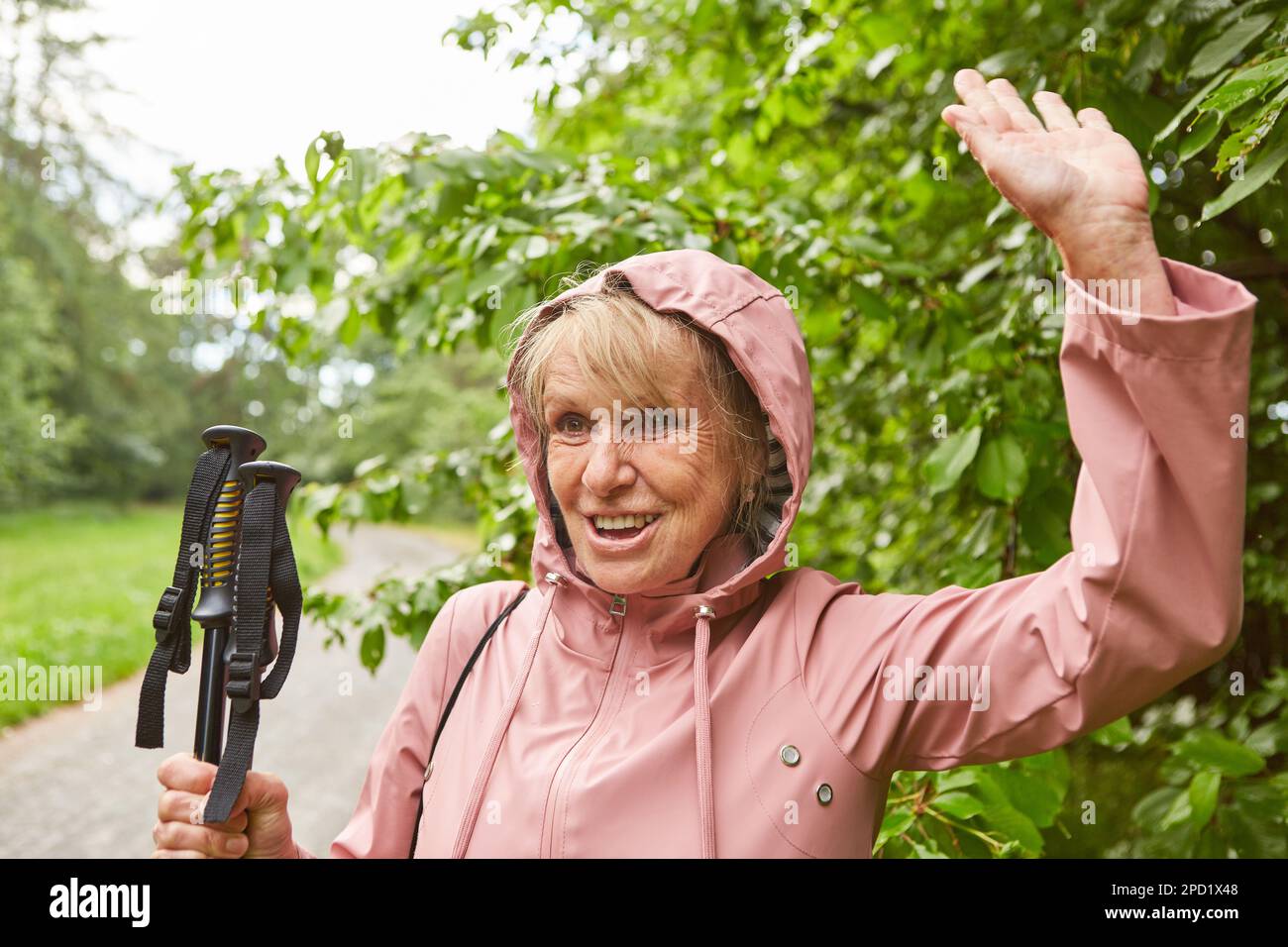 Bonne femme âgée en veste tenant des bâtons de randonnée tout en agitant la main pendant les vacances Banque D'Images