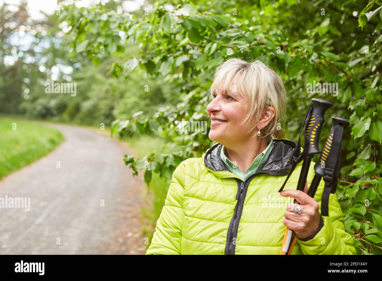 Femme aînée souriante dans des bâtons de randonnée en veste tout en regardant loin pendant les vacances Banque D'Images