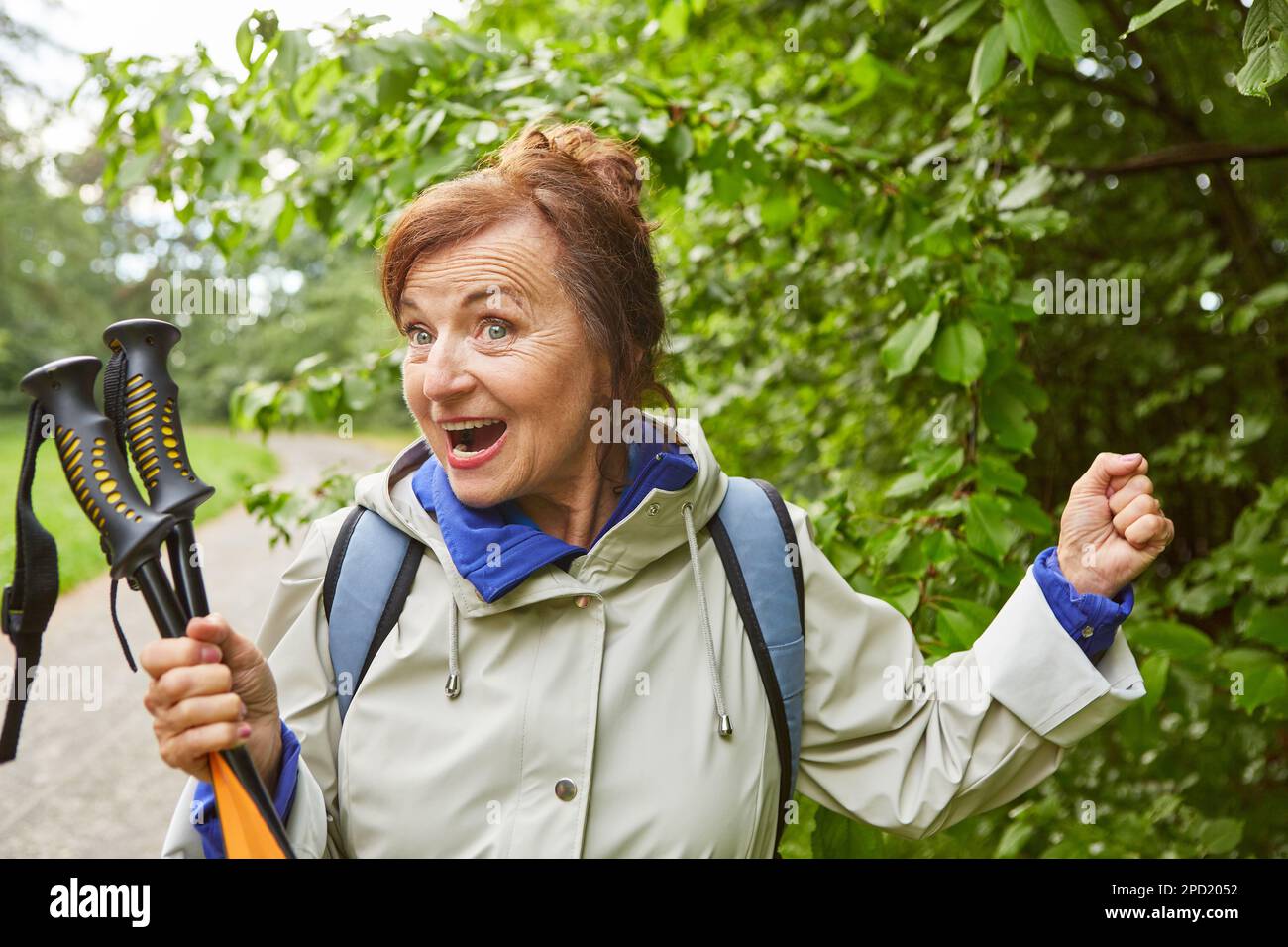 Femme âgée gaie tenant des bâtons de randonnée en veste pendant les vacances Banque D'Images