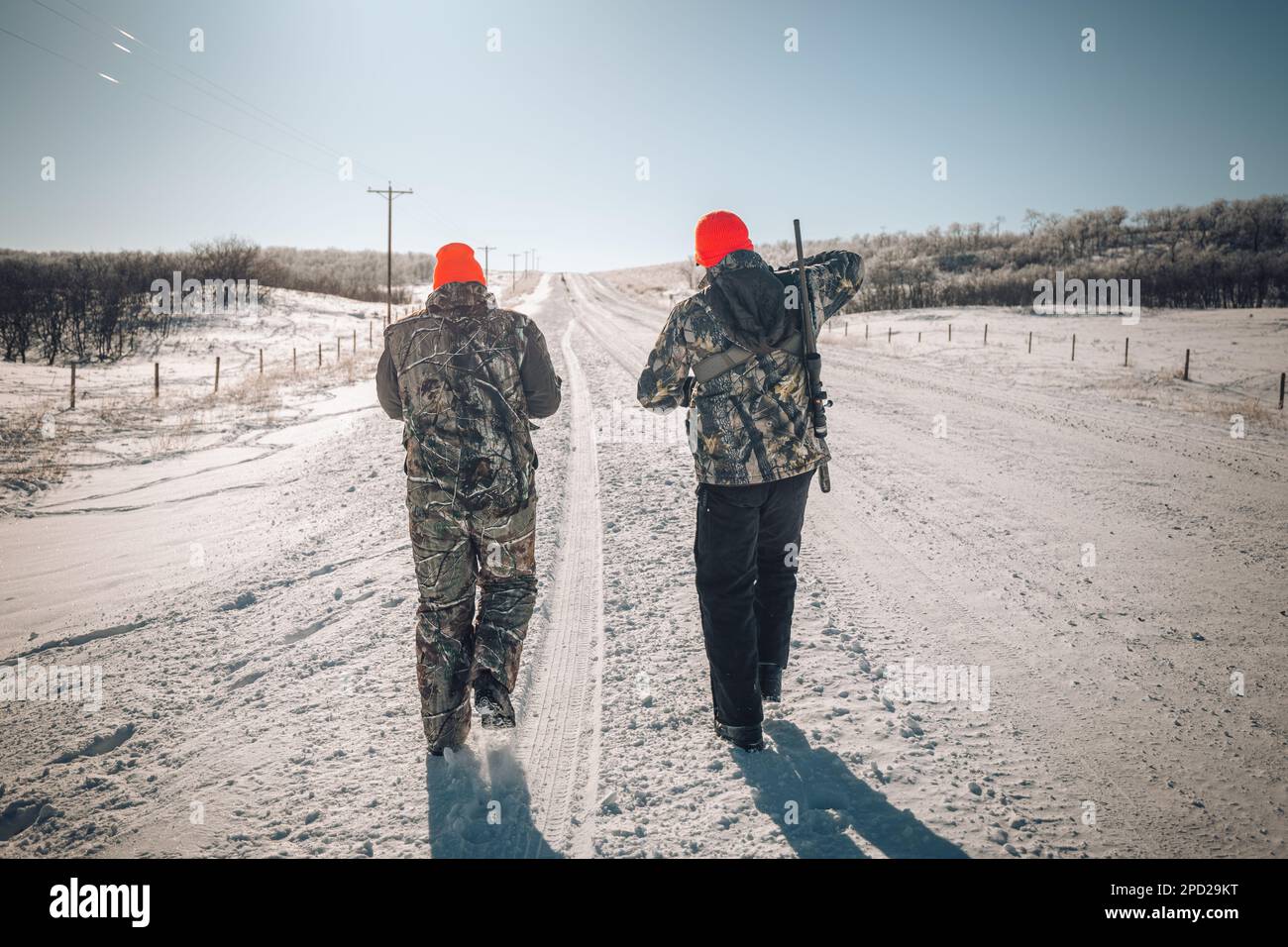 Deux chasseurs mâles portant des casquettes brunes et de lourds vêtements d'hiver marchant ensemble dans une forêt enneigée, Banque D'Images