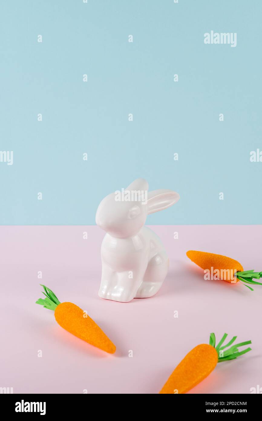 Lapin blanc avec carottes sur fond clair. Concept de vacances de Pâques minimaliste rose pastel et bleu. Banque D'Images