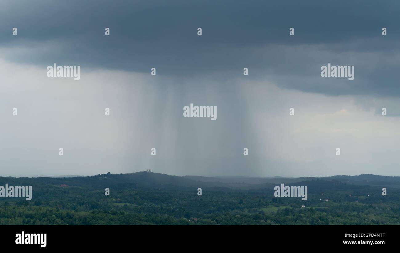 Nuage foncé avec rideau de pluie sur la campagne, nuages éclatent sur un terrain vallonné avec forêt luxuriante et village dispersé Banque D'Images