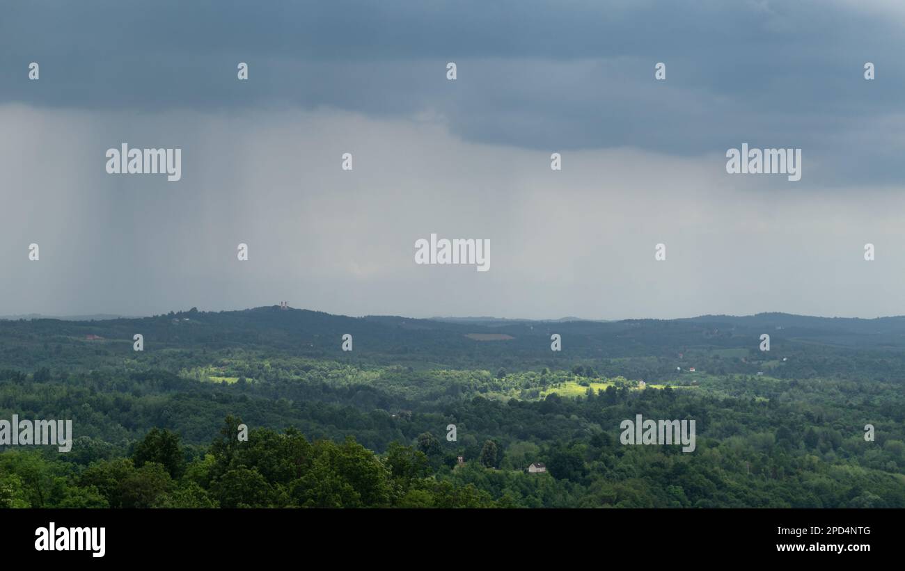 Un nuage surmonte la campagne vallonnée et les taches de soleil sur la forêt et le village dispersé Banque D'Images