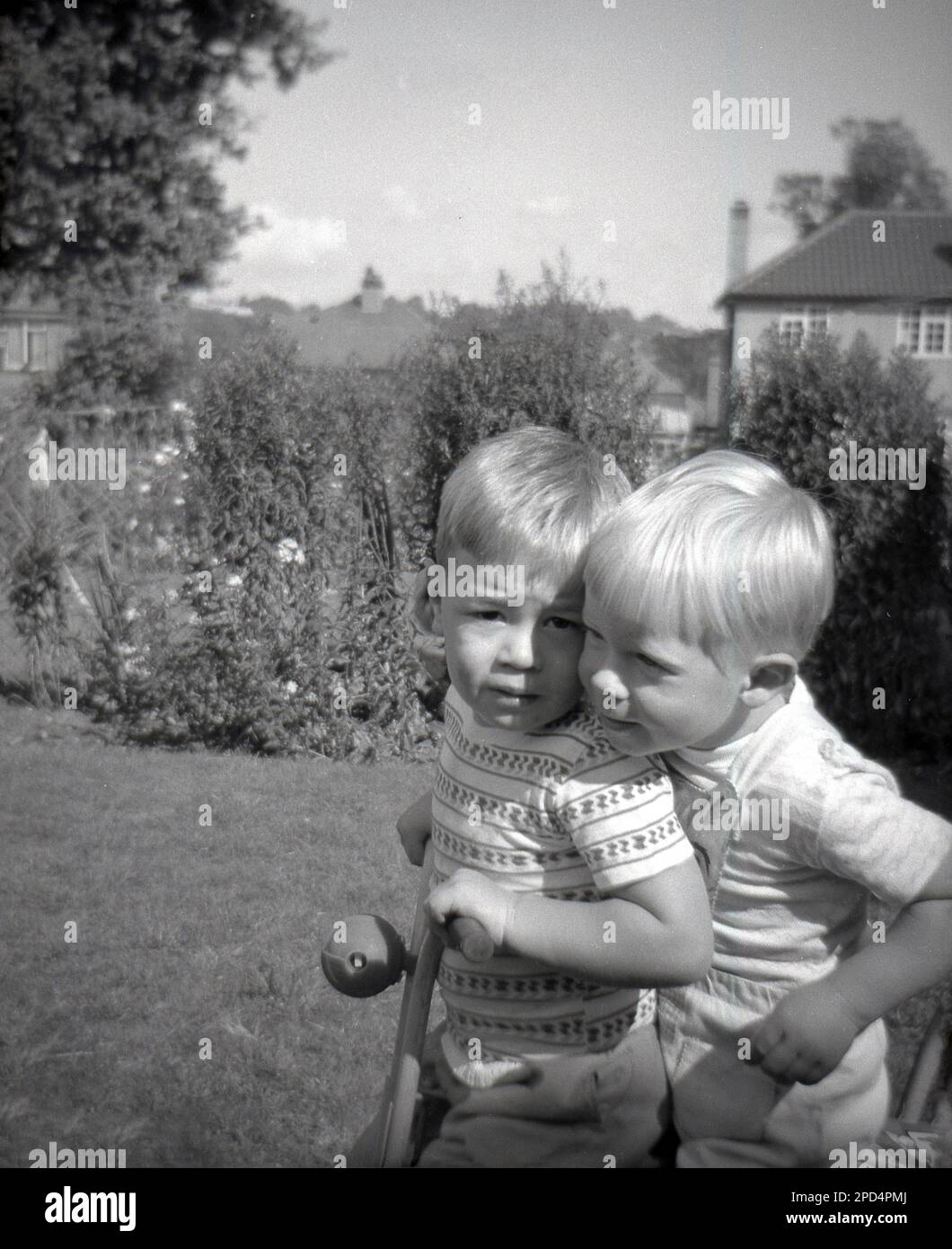 1964, historique, l'été, à l'extérieur dans un jardin, deux petits garçons blonds aux cheveux assis ensemble sur un tricycle d'enfant, Angleterre, Royaume-Uni. Banque D'Images