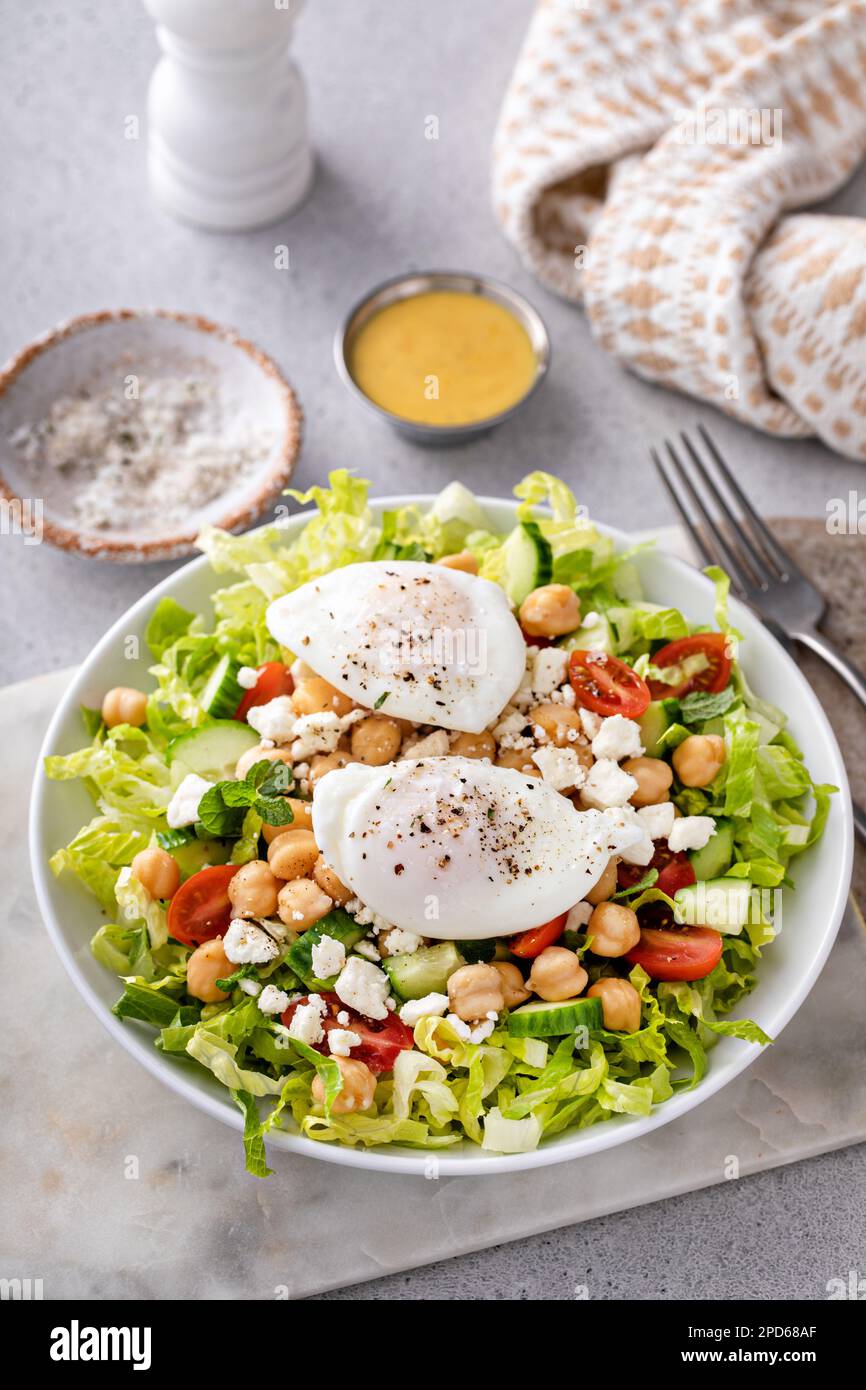 Salade de légumes frais avec pois chiches et feta nappés d'œufs pochés, idée petit déjeuner Banque D'Images