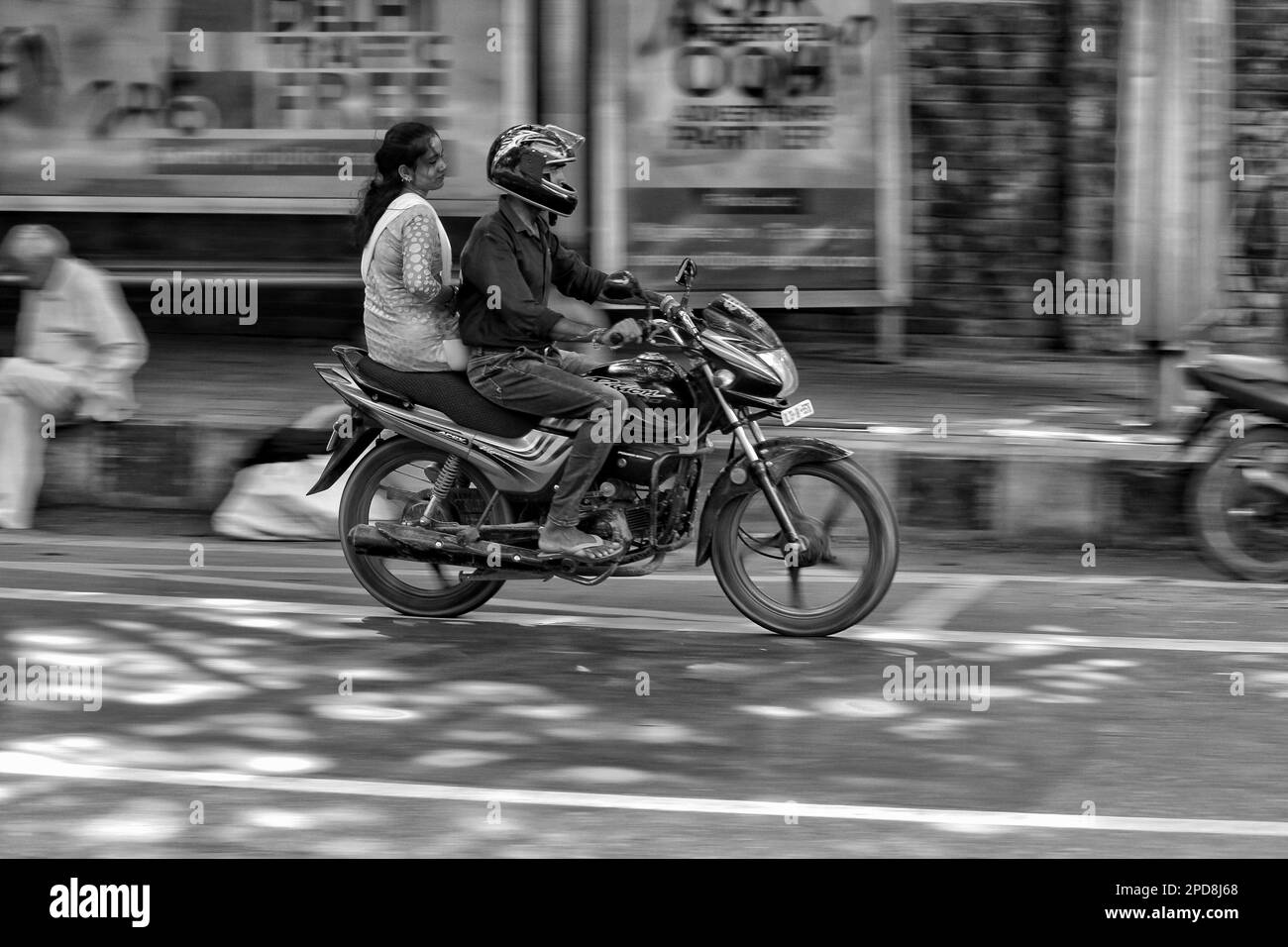 Deux personnes sont vues voyager sur des motos dans une rue de la ville, avec quelques piétons marchant sur le trottoir Banque D'Images