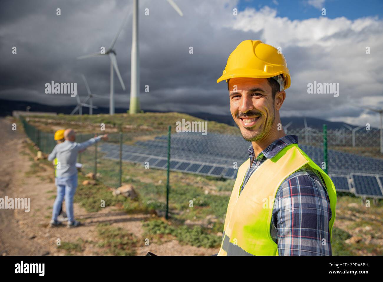 Gros plan d'un ingénieur souriant dans une ferme solaire avec ses collègues en arrière-plan Banque D'Images
