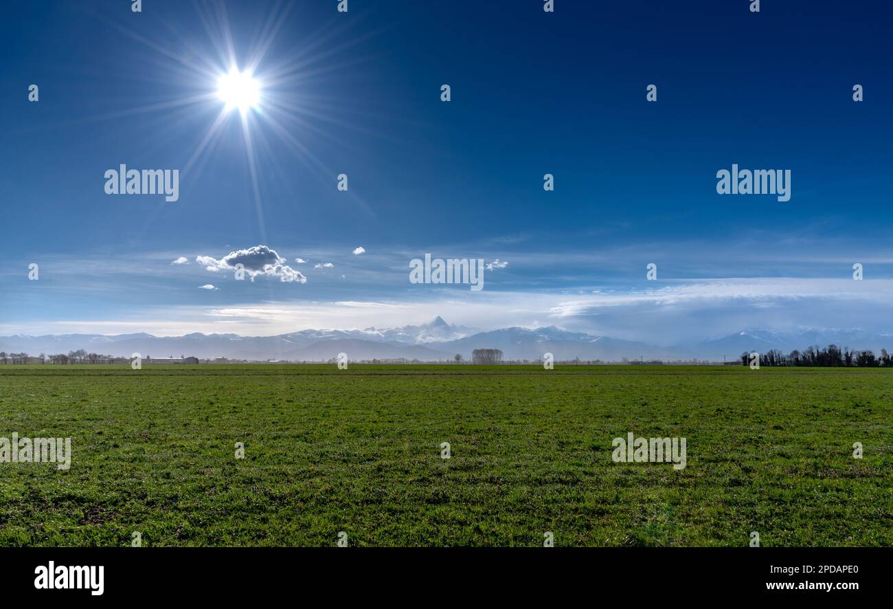 Paysage de prairies verdoyantes dans la haute vallée du po, Piémont, Italie, avec le Mont Monviso dans les nuages en arrière-plan avec ciel bleu et soleil Banque D'Images