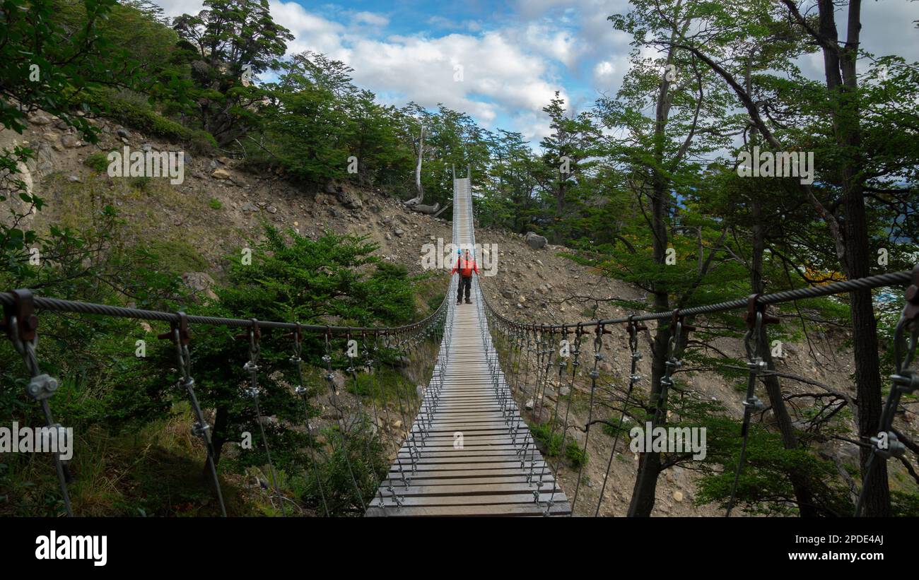 Jeune touriste avec sac à dos vu de l'avant traversant un pont suspendu entouré d'arbres par une journée ensoleillée Banque D'Images