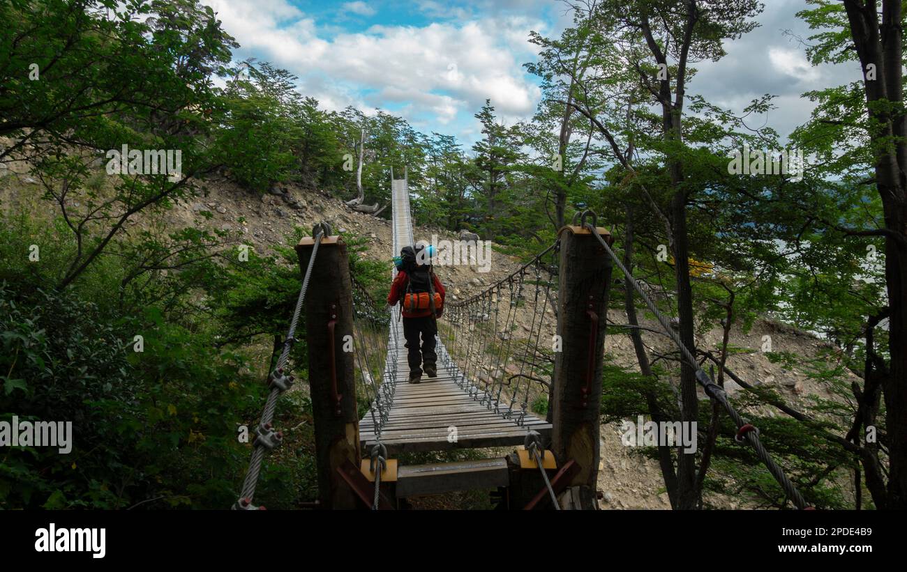 Jeune touriste avec sac à dos vu de l'arrière traversant un pont suspendu entouré d'arbres par une journée ensoleillée Banque D'Images