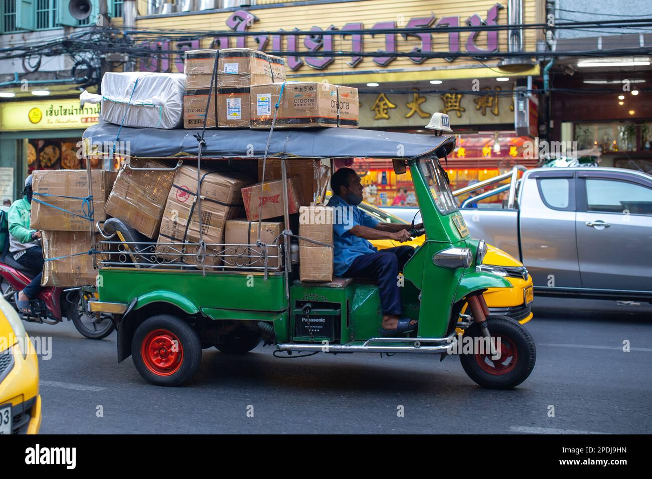 Bangkok, Thaïlande - 19 janvier 2023 : un homme non identifié conduit un tuk-tuk complètement chargé dans les rues de Bangkok. Banque D'Images