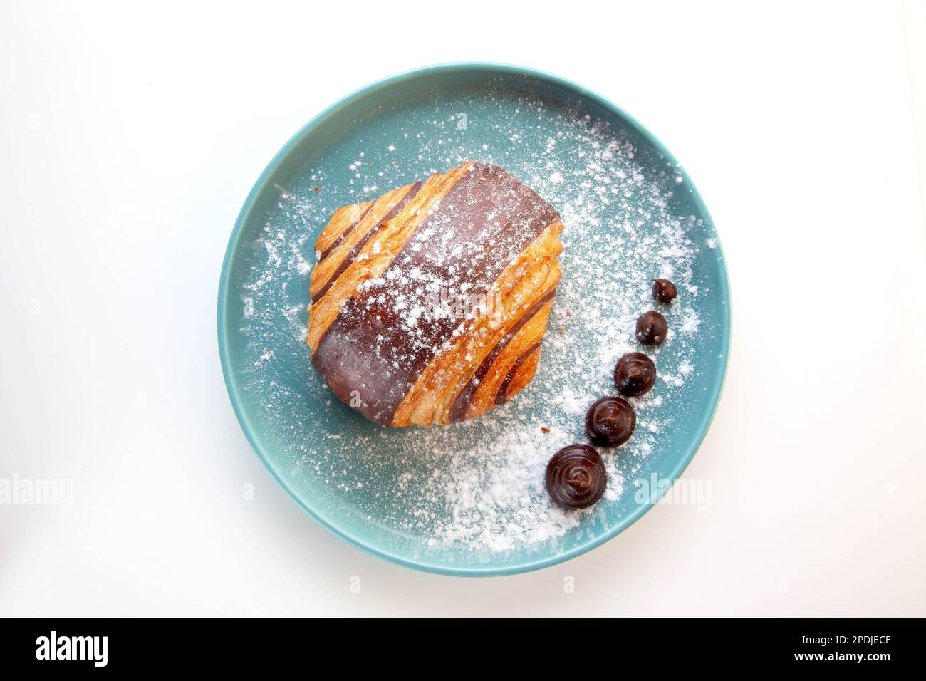 Croissant au chocolat brioche servi sur une assiette bleue. Banque D'Images