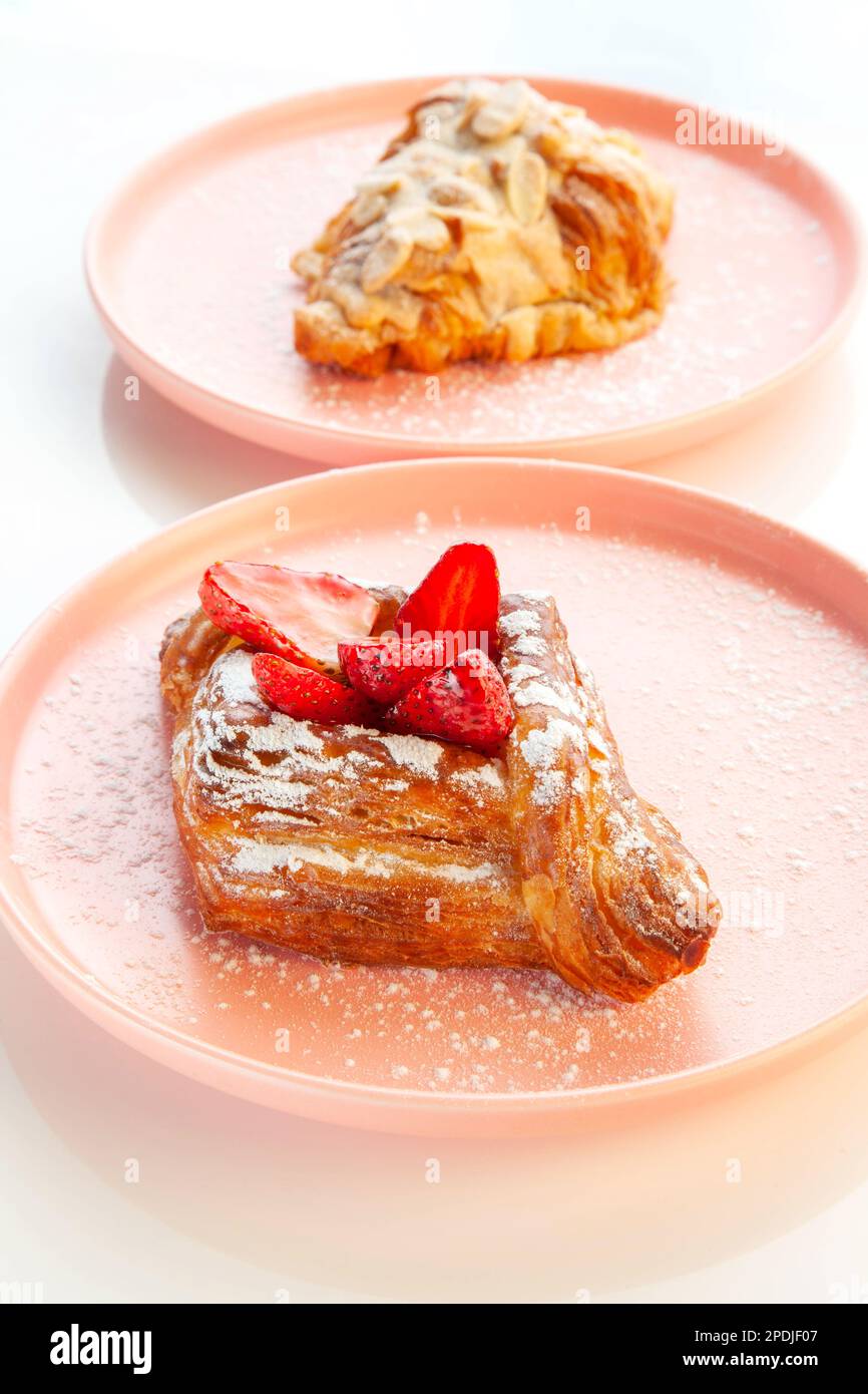 Pâtisserie danoise aux fraises placée sur une assiette rose avec croissant aux amandes en arrière-plan. Banque D'Images