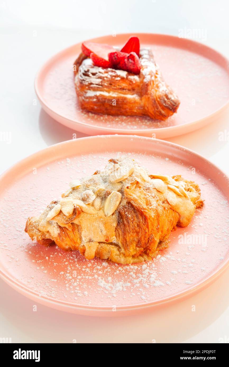 Croissant d'amande placé sur une assiette rose avec des fraises danoises en arrière-plan. Banque D'Images