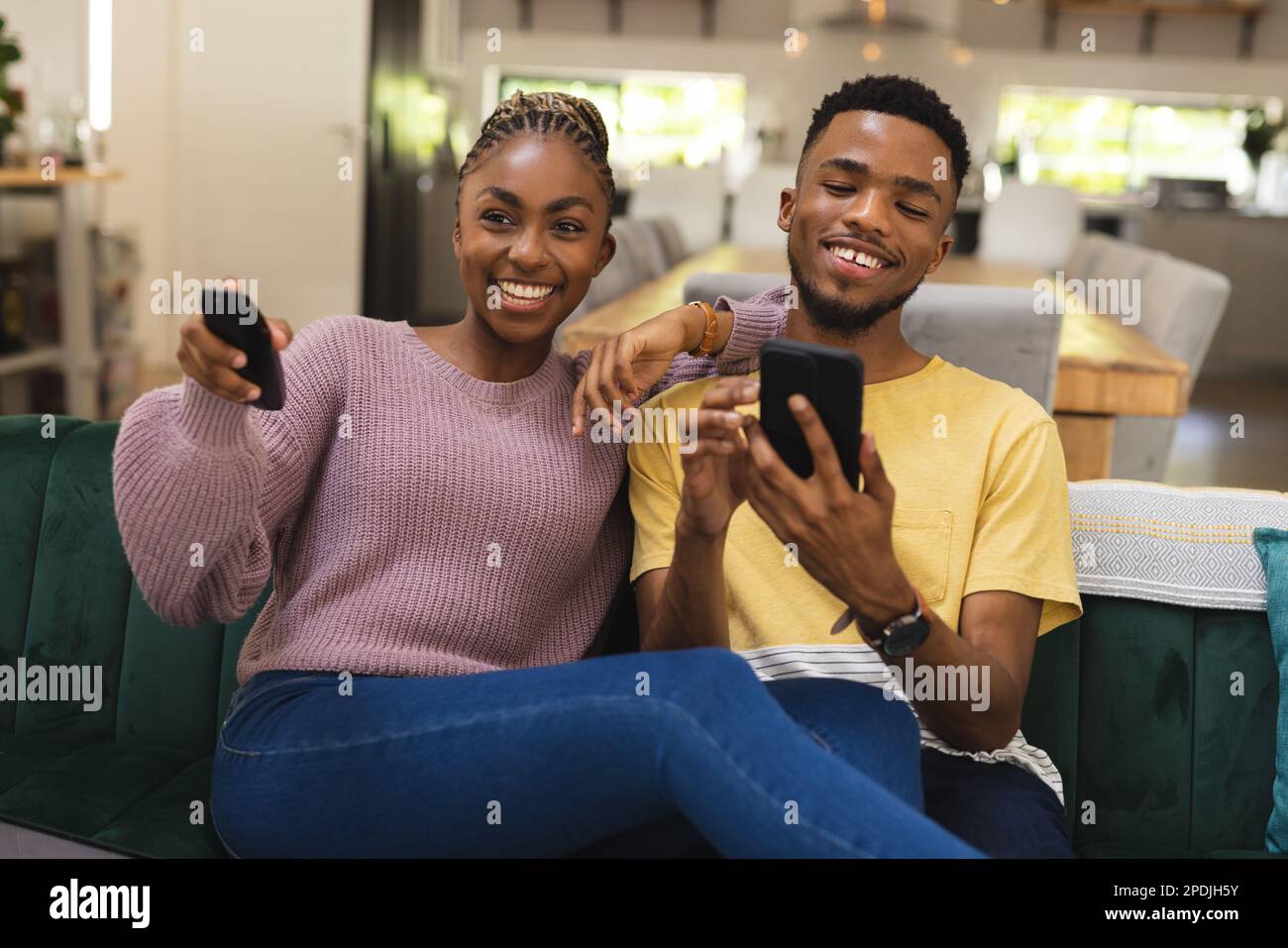 Heureux couple afro-américain assis sur un canapé et utilisant un smartphone Banque D'Images