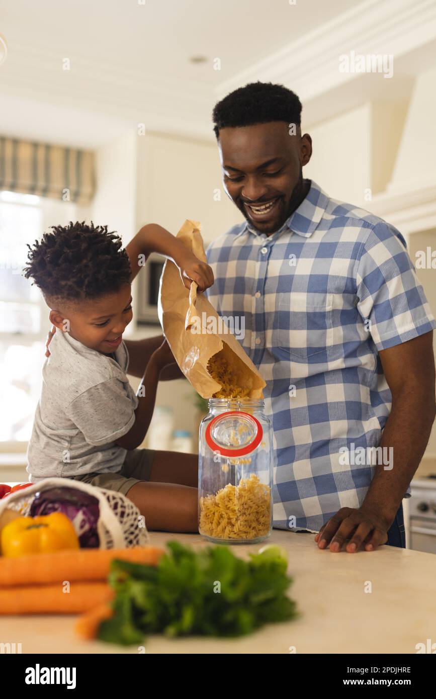 Un père et un fils afro-américains heureux qui déballe ses produits d'épicerie dans la cuisine Banque D'Images