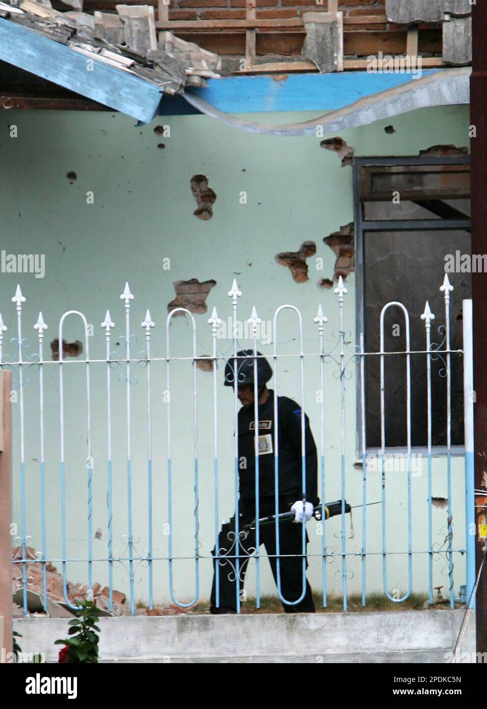 A member of Indonesian Police bomb squad searches the house where gunfight between police and terrorist suspects occured on Wednesday as bullet-riddled wall is seen on the background, in Batu, East Java, Indonesia, Thursday, Nov. 10, 2005. Malaysian terror leader Azahari bin Husin was believed to have been killed in the shootout. (AP Photo /Dita Alangkara) Banque D'Images