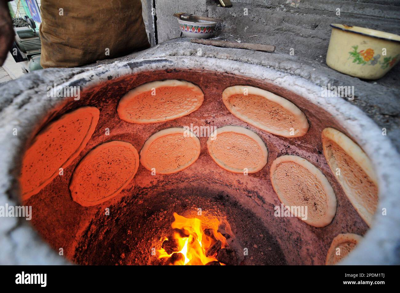 Un Uyghur cuisant le pain Naan dans un four tandoor dans la vieille ville de Kashgar, Xinjiang, Chine. Banque D'Images