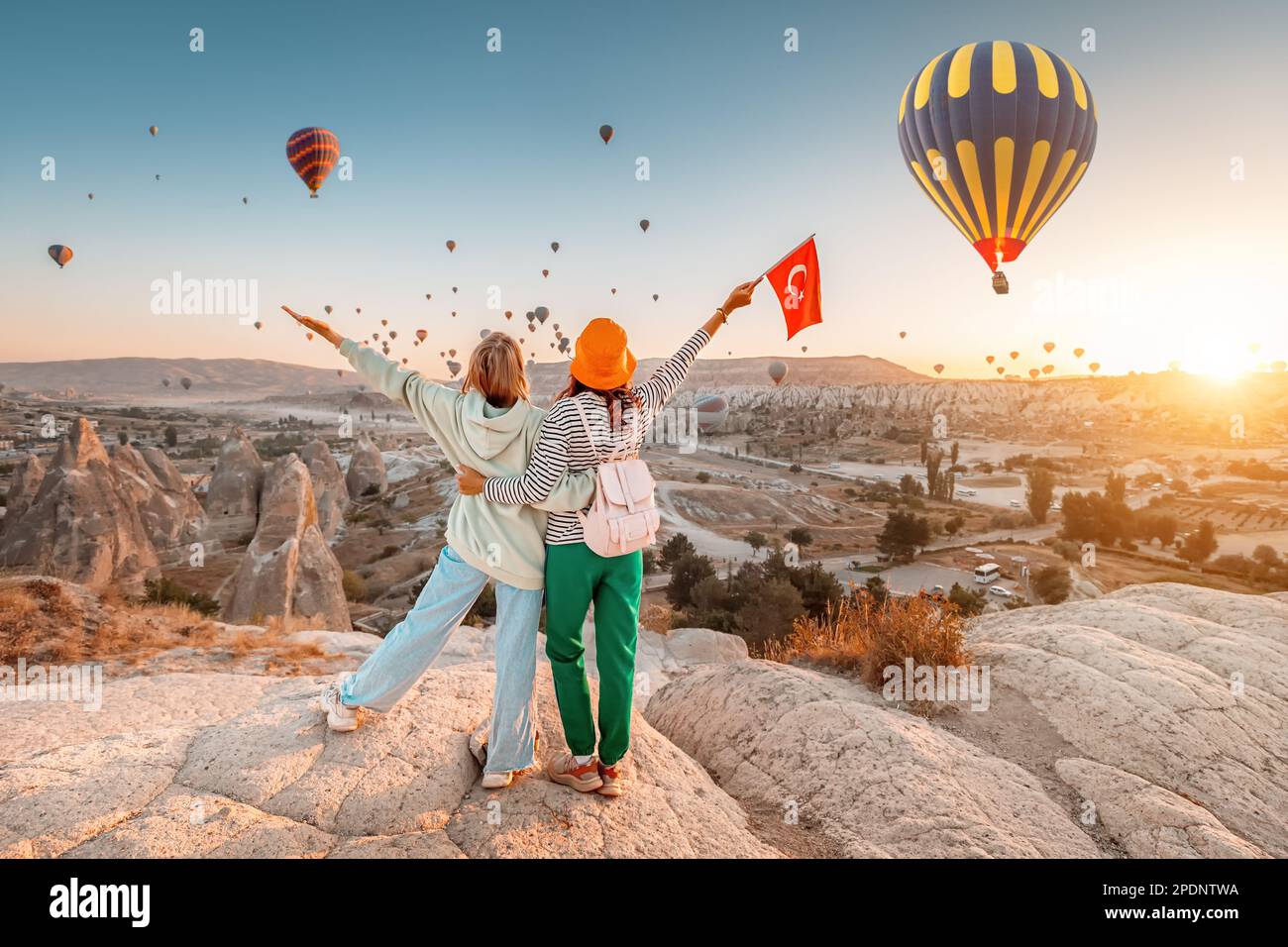 Les filles amis voyageurs avec le drapeau turc, embrassant sur un point de vue et en admirant la vue des ballons d'air chaud volant en Cappadoce Banque D'Images