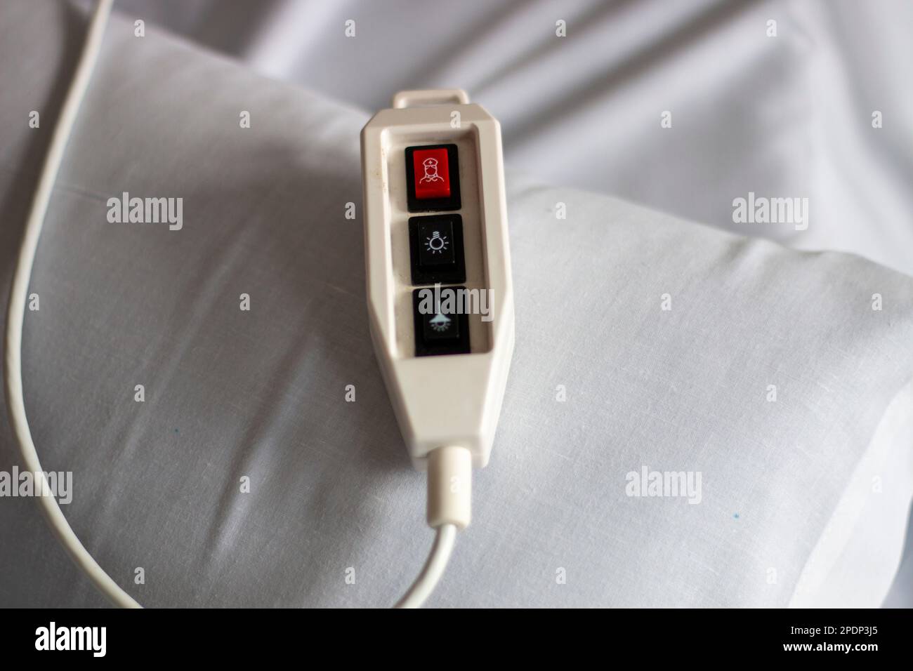 Contrôle d'appel de l'hôpital avec un bouton d'urgence rouge reposant sur un lit avec des draps blancs Banque D'Images